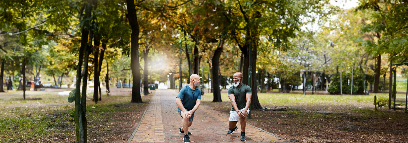 Two mature men stretching before their morning run in the park.