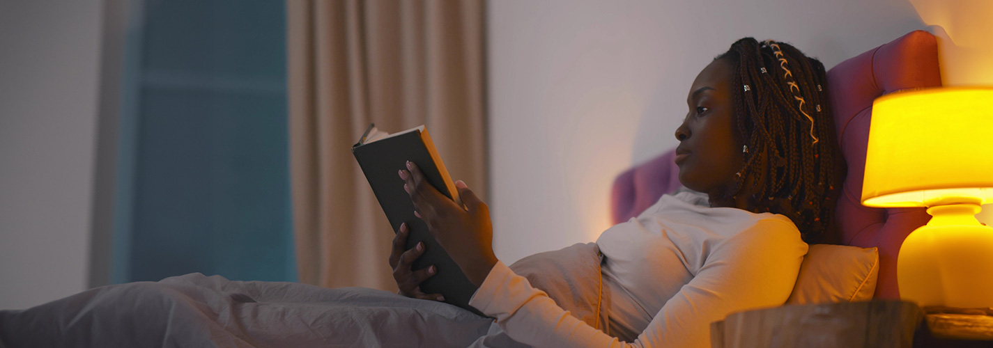 A young african-american woman reads a book in bed, before going to bed.