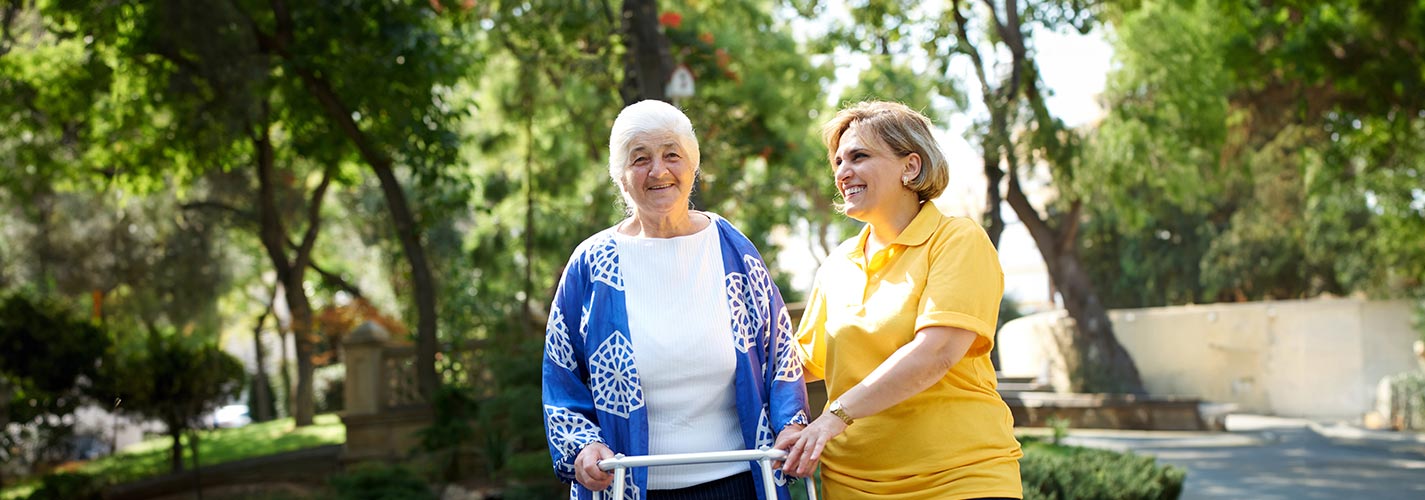 A smiling senior woman and her home health aide take a short walk together.