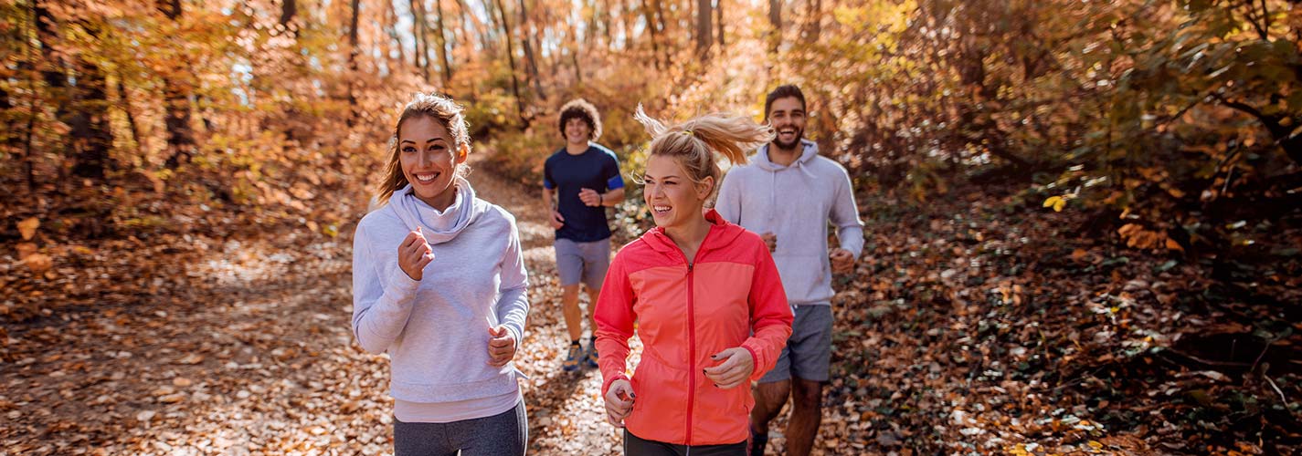 A group of friends jog on a wilderness trail surrounded by beautiful orange fall folliage.