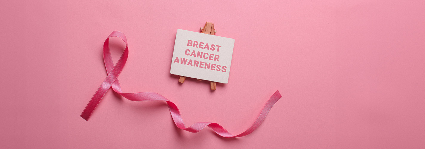 A pink ribbon and a miniature easel against a light pink background. The easel reads "Breast Cancer Awareness"