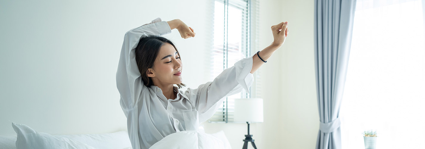 A young smiling woman, wakes up and stretches in the morning.