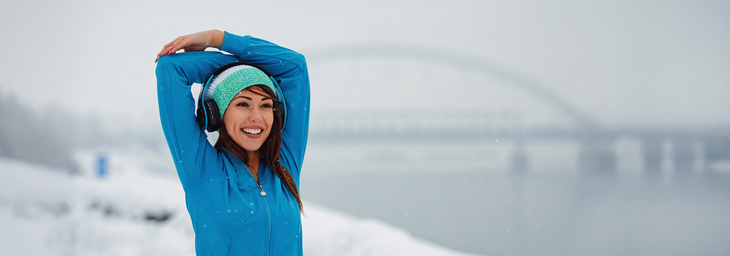 A young woman stretching her arms before her run, on snowy day in the city.