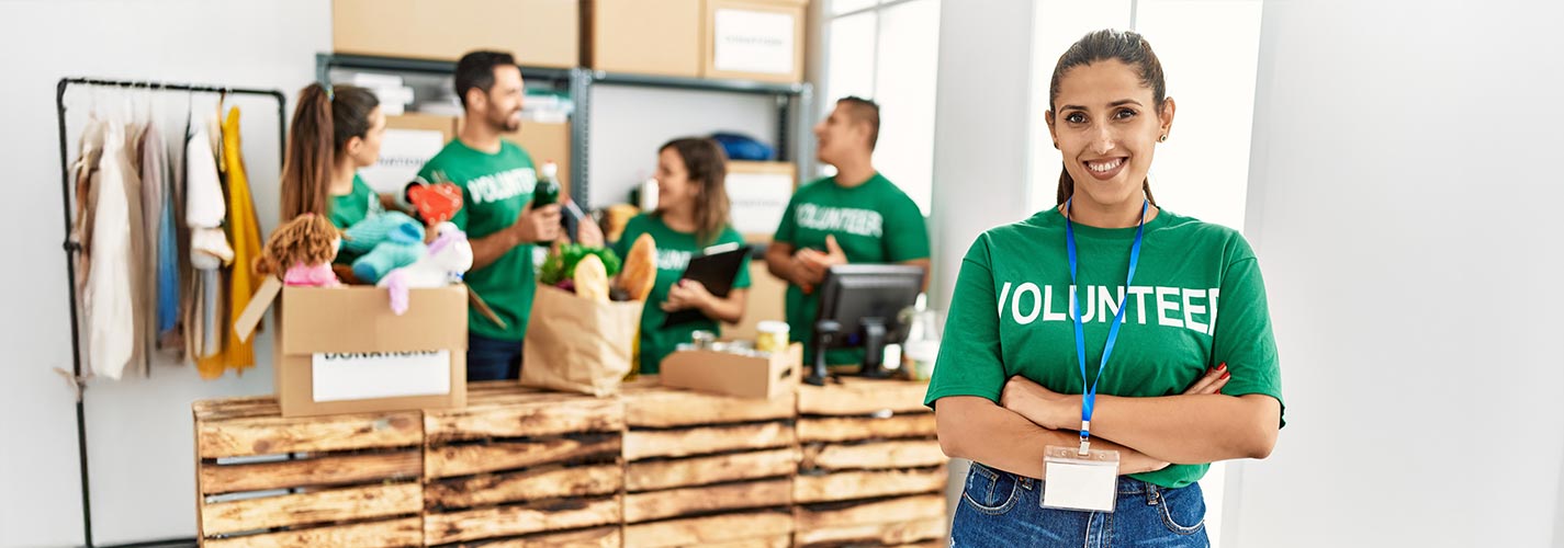 A group of young volunteers working at charity center with a woman in the front smiling, standing with arms crossed gesture.