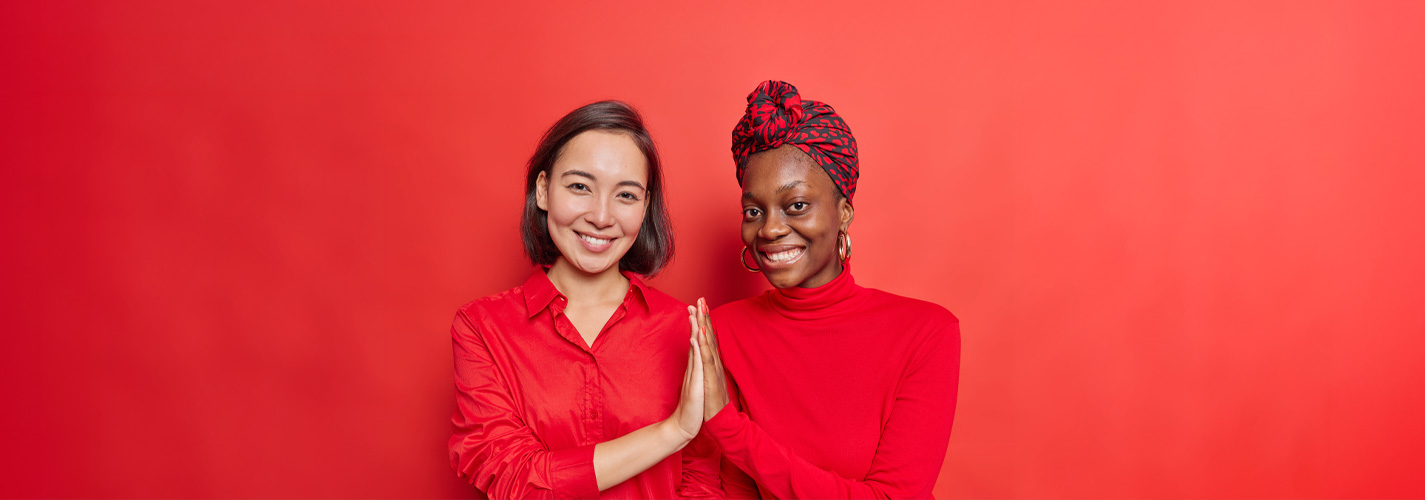 Two young women wearing red against a red background press their palms together in a show of mutual support.